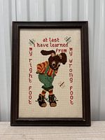 Full view of framed cross stitch with bunny and embroidered text in red, showing the entire artwork with frame.