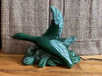 Side view of the ceramic duck figurine in teal green glaze showing the figurine's shape and detailing.