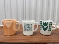 Front view of three vintage milk glass mugs showing designs: peach lustre, blue-grey atomic, and green tulip plaid.