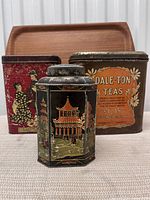 Front view of three vintage tea tins arranged side-by-side showing detailed artwork and patina.