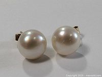 Front view of two round white pearl earrings on a white background showing their lustrous surfaces.