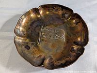 Poppy-shaped solid brass coin or dresser dish with central waving flag etching, showing tarnish and patina.