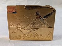 Front view of lighter showing etched ducks flying and landing in marsh scene.