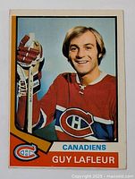 Front image of 1974-75 O-Pee-Chee Guy Lafleur hockey card showing player in Canadiens jersey with hockey sticks.