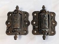 Pair of antique cast iron Gothic hinges showing embossed design and barrel pivot mechanism, front view.
