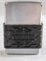 Front view of chrome Zippo lighter with black Harley Davidson rubber wrap, showing some wear and scratches.