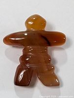 Front view of a polished jade Inukshuk-shaped brooch in amber-brown tones with natural stone color variations.