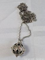 Photo showing the sterling silver hollow spherical ball pendant with intricate black detailing alongside the chain.