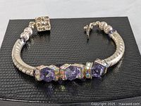 Sterling silver bracelet laid flat on a black textured surface, showing the clasp and decoration side with amethyst and rhinestones.