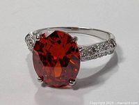 Close-up front angle of the sterling silver ring with large red oval gemstone and small accent stones on the band.