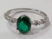 Close-up of front face of sterling silver ring showing green oval gemstone and accent stones on band