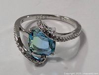 Front angled view showing the aqua blue gemstone centered between swirling sterling silver arms adorned with small clear stones.