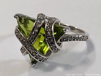 Close-up angled view of the sterling silver ring showcasing the green triangular stone and the entwined design with small dark stones.