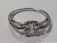 Sterling silver ring with square-cut clear tourmaline and small accent stones on band shown on white background from front view.