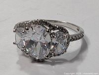 Close-up of sterling silver ring with a large clear oval faceted stone, two smaller oval clear stones, and small accent stones on the band, showing front view.