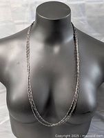 Front view of the triple strand necklace displayed long on a black bust form.