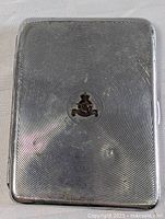 Front view of metal cigarette case showing concentric circle design and small colored RCAF emblem at center.
