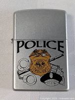 Front view of the vintage Zippo police lighter showing clear police badge, revolver, handcuff, and cap graphics on silver-tone metal body.