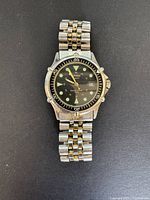 Front view of the watch showing the metal band, black face with prominent luminous markers, and rotating bezel.