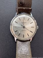 Front view of a vintage Cardinal men's wristwatch with a silver dial and brown leather strap showing some wear and a scratched crystal.