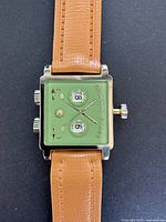 Full front view of square gold-tone watch with green dial and tan leather strap