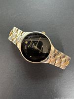 Front angled view of watch showing black dial with diamond markers and Gruen branding near top and bottom, with metal band and scratched crystal surface.