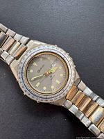 Front angled view of vintage Rochelle watch showing grey dial with luminous markers, day-date window, gold-tone second hand, and silver-gold metal band.