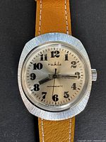 Front view of vintage Ruhla wristwatch with tan leather strap and silver-brushed round case showing large black numbers on dial and black hands, 'Ruhla' branding visible.