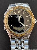 Front close-up showing black dial with silver hour markers and hands, digital display at 6 o'clock, worn gold-tone bezel on a stainless steel case.