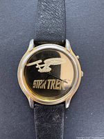 Front view of vintage Star Trek men's watch with black leather strap. Shows silhouette of USS Enterprise and Star Trek logo on dial.
