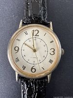 Front view of vintage men's manual wind wristwatch showing white dial with mixed gold-tone Arabic and black Roman numeral hour markers, gold-tone hands, '17 Jewels' mark on dial and black crocodile pattern leather strap.