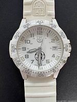 Front view showing white dial, Arabic numerals, date window, and white rubber strap.