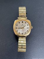 Front view of vintage gold-tone Invicta men's wristwatch with silver dial showing date window and expansion band.