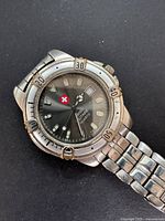 Front view of the wristwatch showing black dial, red Swiss cross logo, luminous markers, rotating bezel with minute markers, and stainless steel link bracelet.