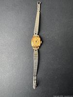 Full view of the vintage women's Cardinal watch with gold-tone rectangular case and metal band laid flat on black background.