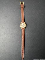 Full length photo of the vintage women's wristwatch showing gold-tone case and brown leather strap.