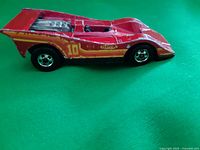 Side view of red Hot Wheels race car with number 10 decals and rear fins, showing wear and paint chips