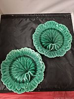 Top view of two green Wedgwood plates shaped like leaves showing veined pattern and curled stem design.