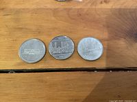 Three Canadian one dollar coins placed side by side on a wooden surface, showing the reverse sides with commemorative designs for 1973, 1982, and 1984 respectively.
