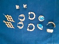 Photo showing all earrings laid out on a blue background, displaying six pairs with various designs and colors.