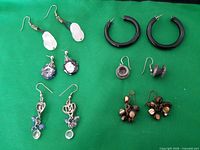 Lot overview showing six pairs of pierced earrings of different styles and materials on green background.