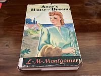 Front cover of the "Anne’s House of Dreams" book showing a woman in a green dress with background scenery, with worn and torn dust jacket edges.