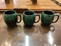 Front view of three green Blue Mountain Pottery mugs placed side by side showing rounded shape and handles.