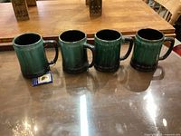 Four Blue Mountain Pottery mugs in green gradient on display, shows four items for sale.