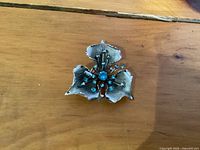 Front view of Bond Boyd sterling silver flower brooch with turquoise stones on wooden surface.