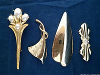 Four vintage brooches arranged on fabric background, showing details of each piece including pearls and rhinestones.