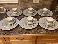 6 place settings displayed showing arrangement of plates, cups, and saucers on a countertop.