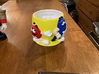 Photo of the front side showing Red and Blue M&M's characters on the yellow candy dish.