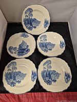 Top view of five side plates arranged on a surface, showcasing detailed blue pastoral landscape with scalloped edges and dark blue rim trim.
