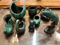 Overview of green glazed pottery items including fish pitcher, shoe planter, small owl figurine, and various vases and pitchers.